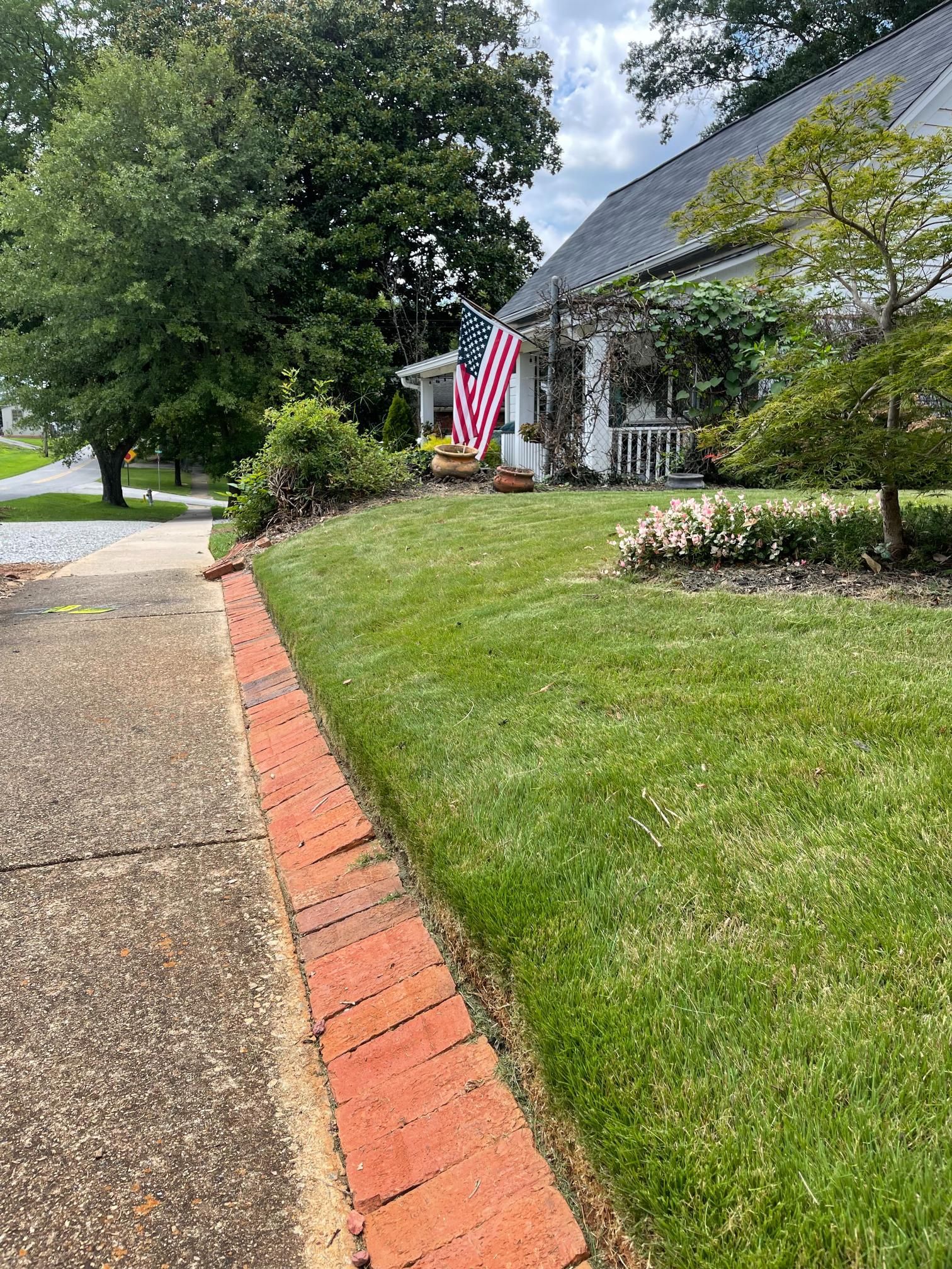 A brick walkway leading to a house with a lush green lawn.