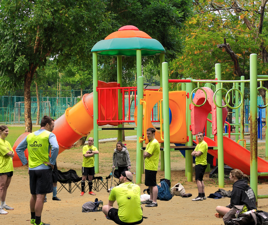 A group of people wearing neon yellow vests gather in a playground for a meeting or break.
