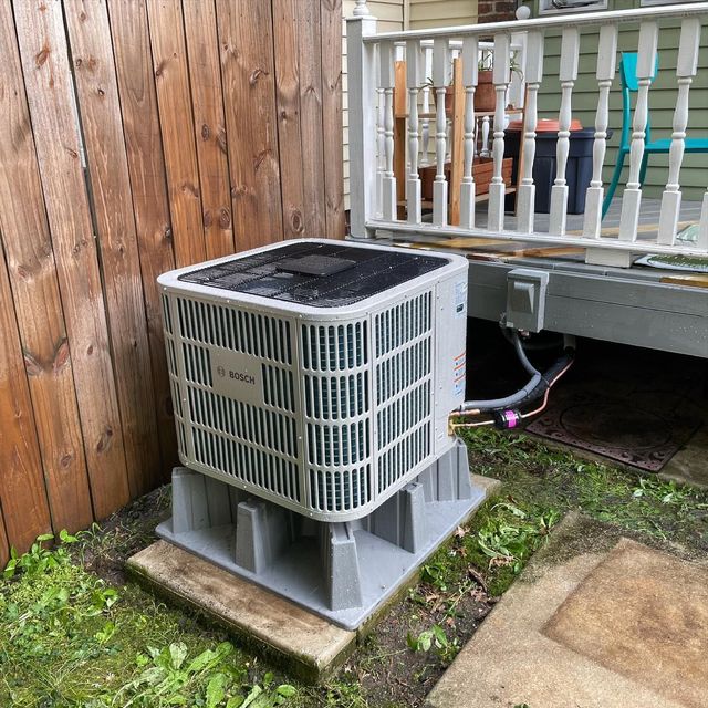 Air conditioning unit on a concrete base next to a wooden fence and a deck.