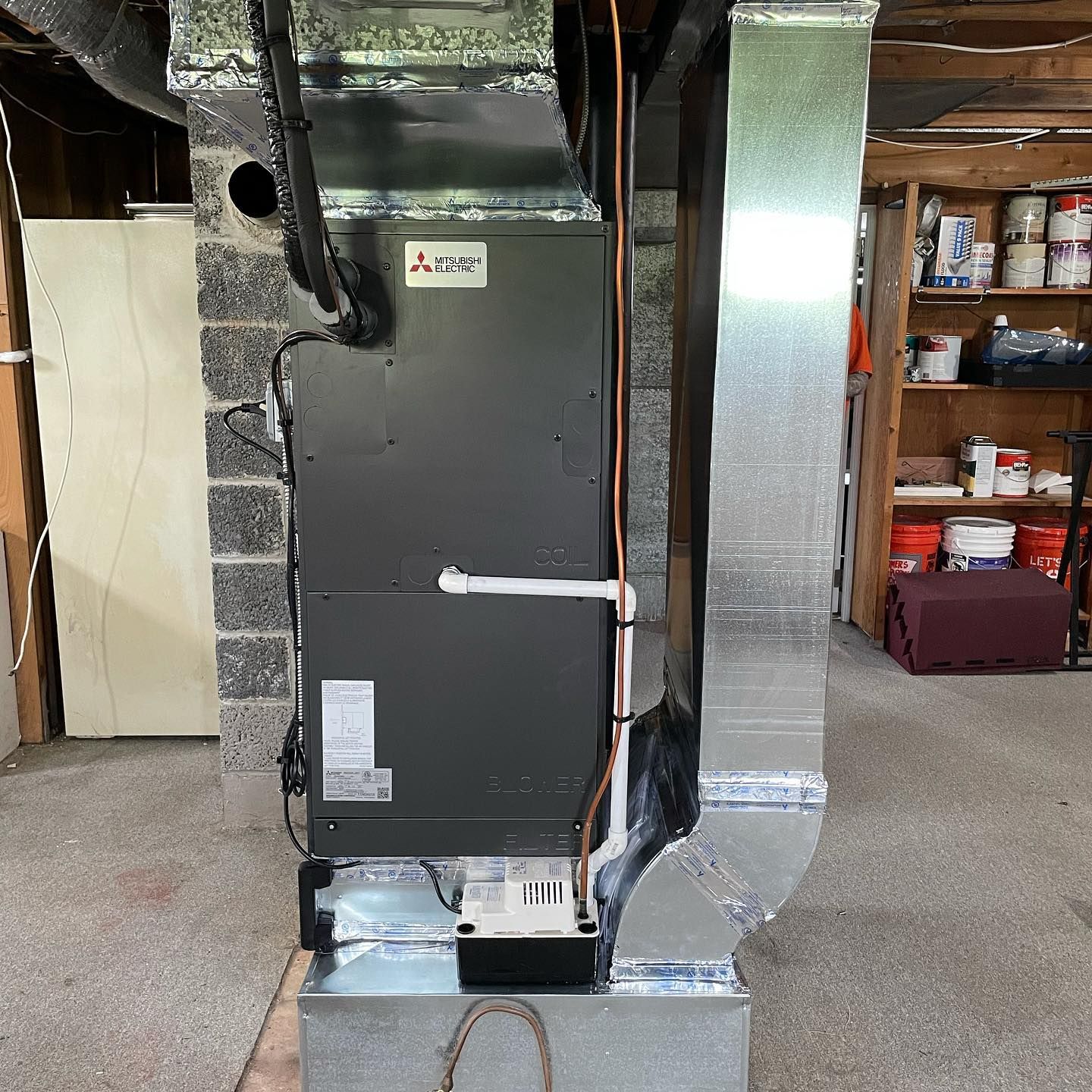Mitsubishi HVAC unit installed in a utility room with ductwork and a white pipe.