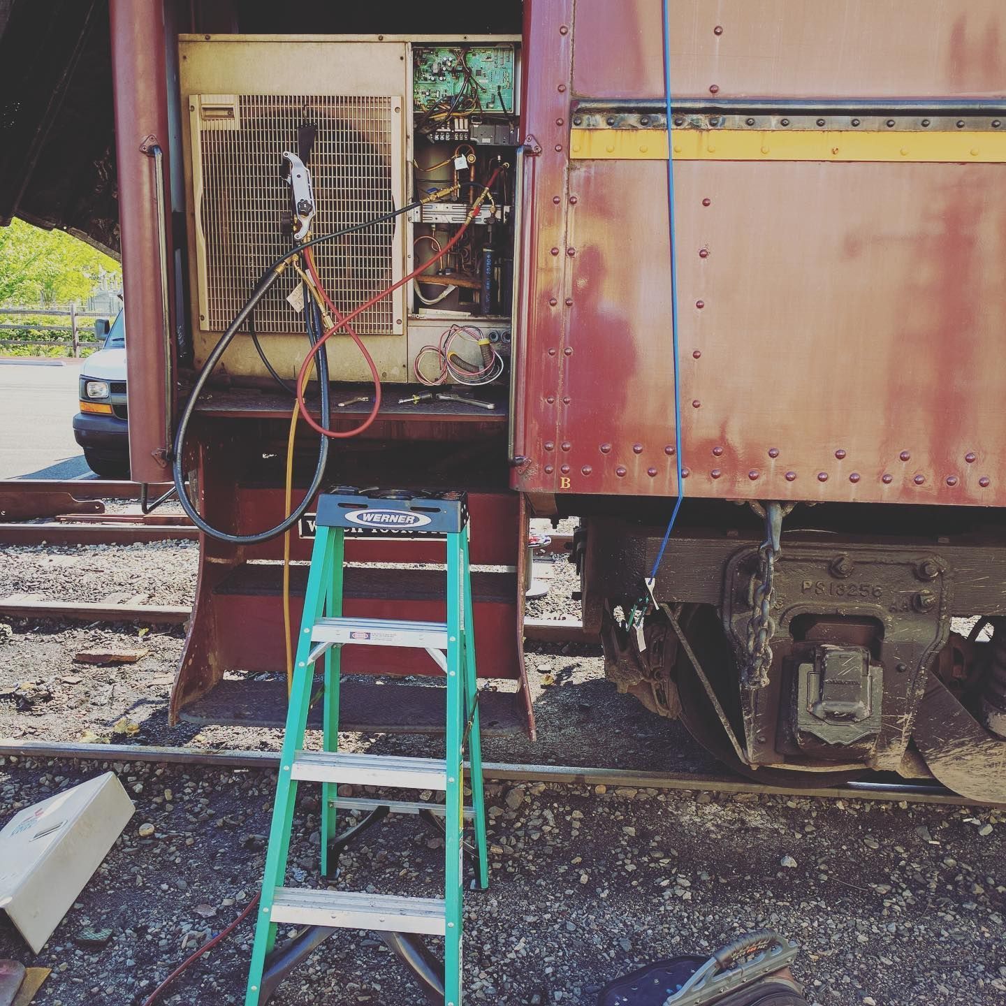 Train car open for repairs, with a ladder and equipment. Exterior, outdoor setting.