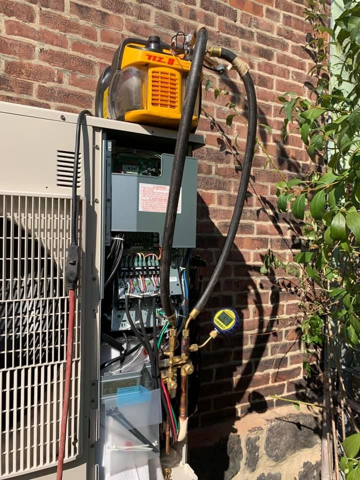 An air conditioning unit being serviced outdoors, with hoses connected to gauges and tools.