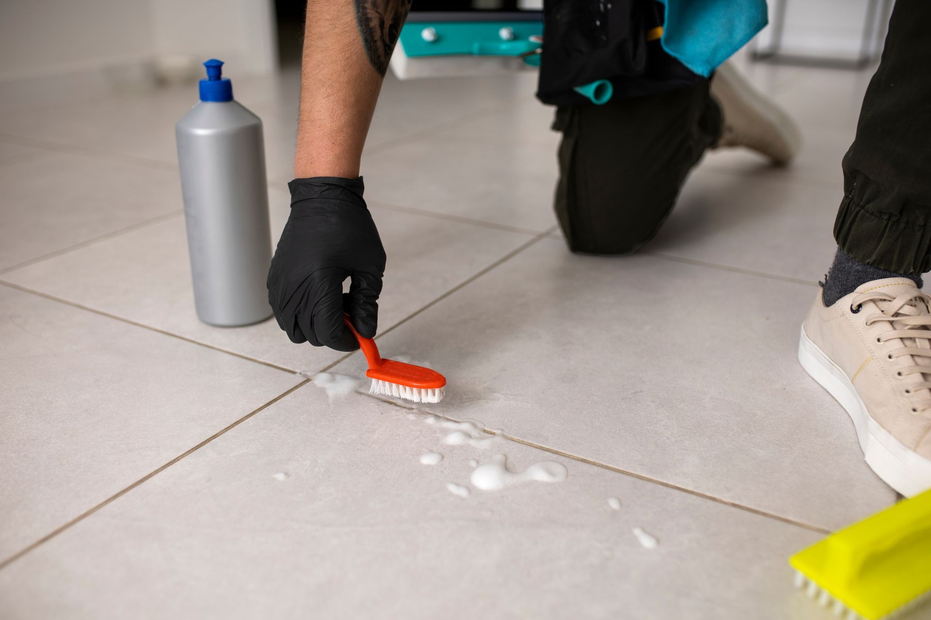 a person wearing black gloves is cleaning the floor with a red brush