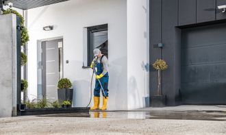 a man wearing yellow gloves is using a high pressure washer outside of a house