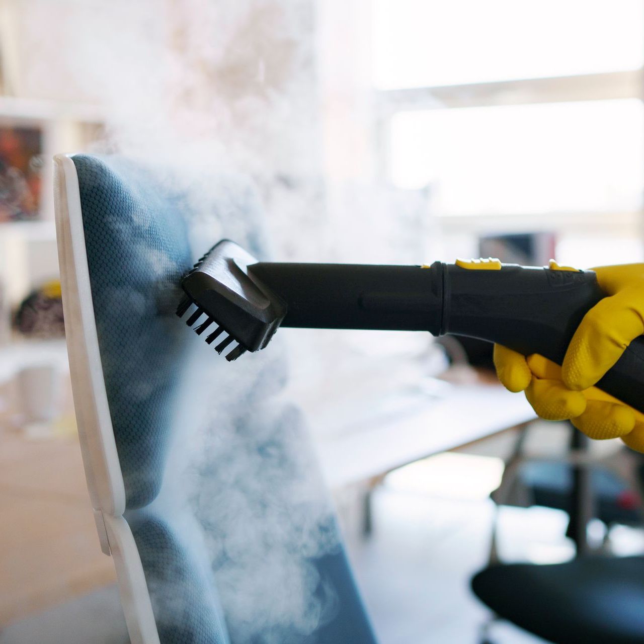 a person wearing yellow gloves is cleaning a chair with a steam cleaner