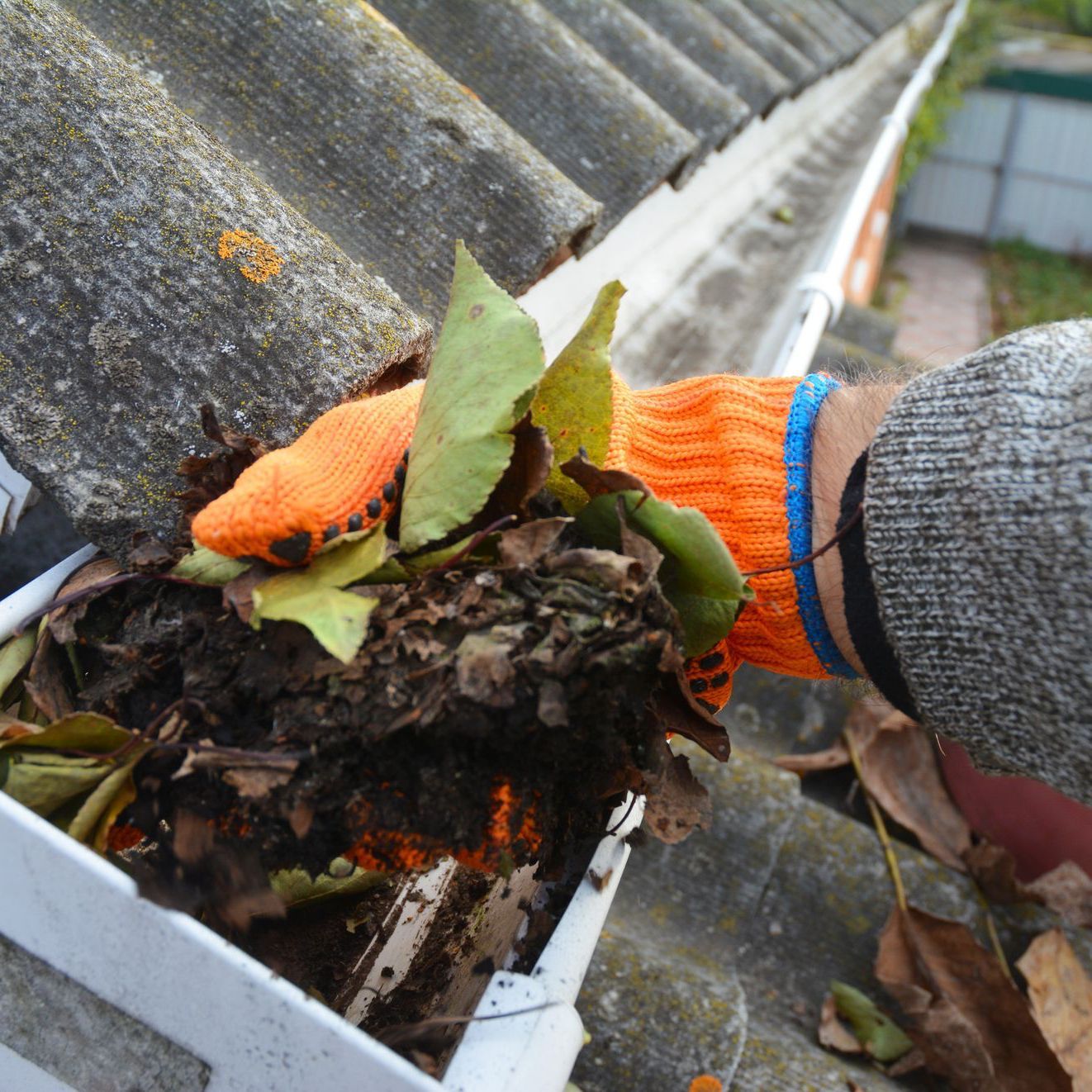 a person wearing orange gloves is cleaning a gutter