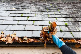 a person wearing a blue glove is cleaning leaves from a gutter