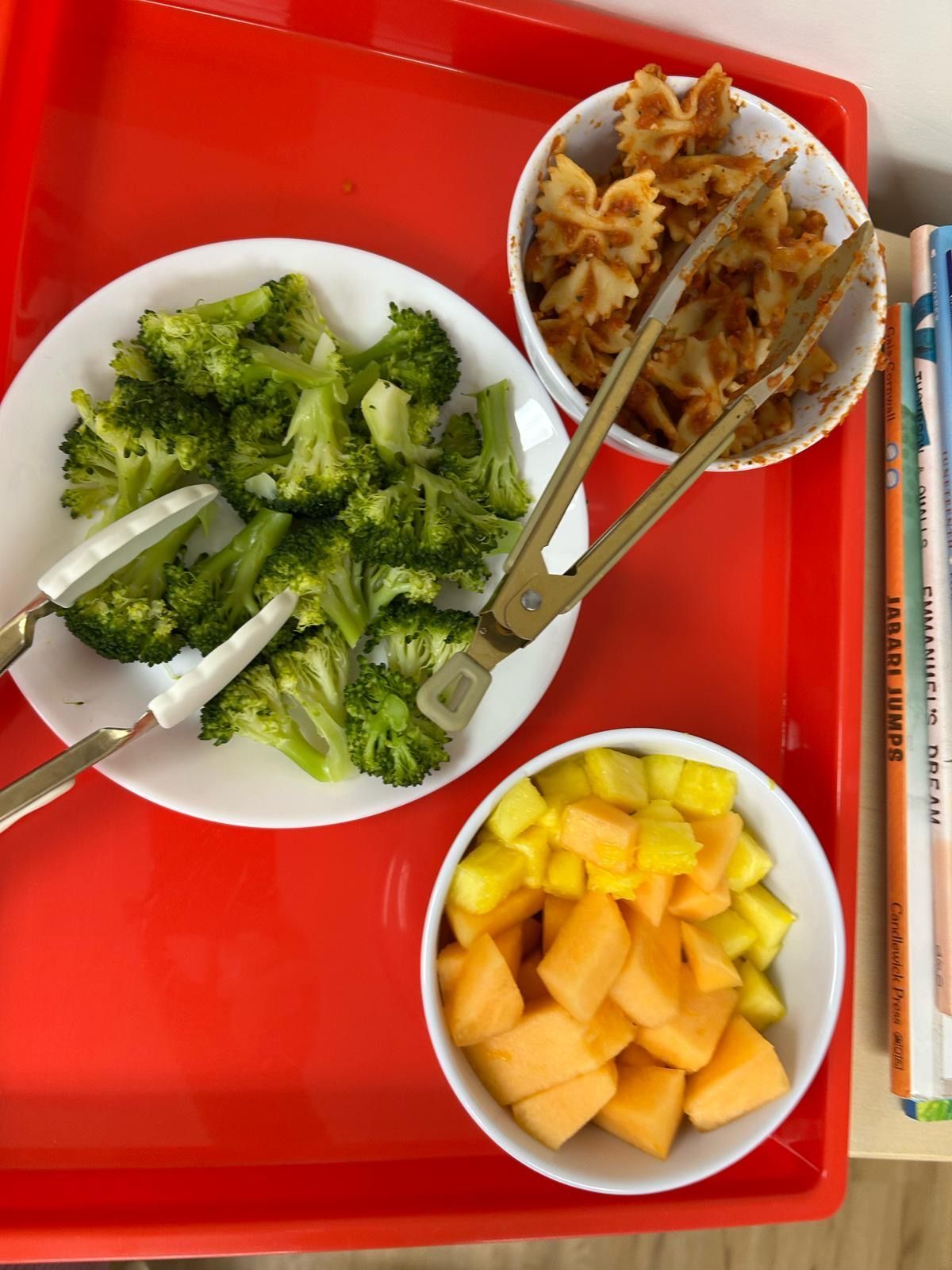 A plate of broccoli pasta and melon on a red tray