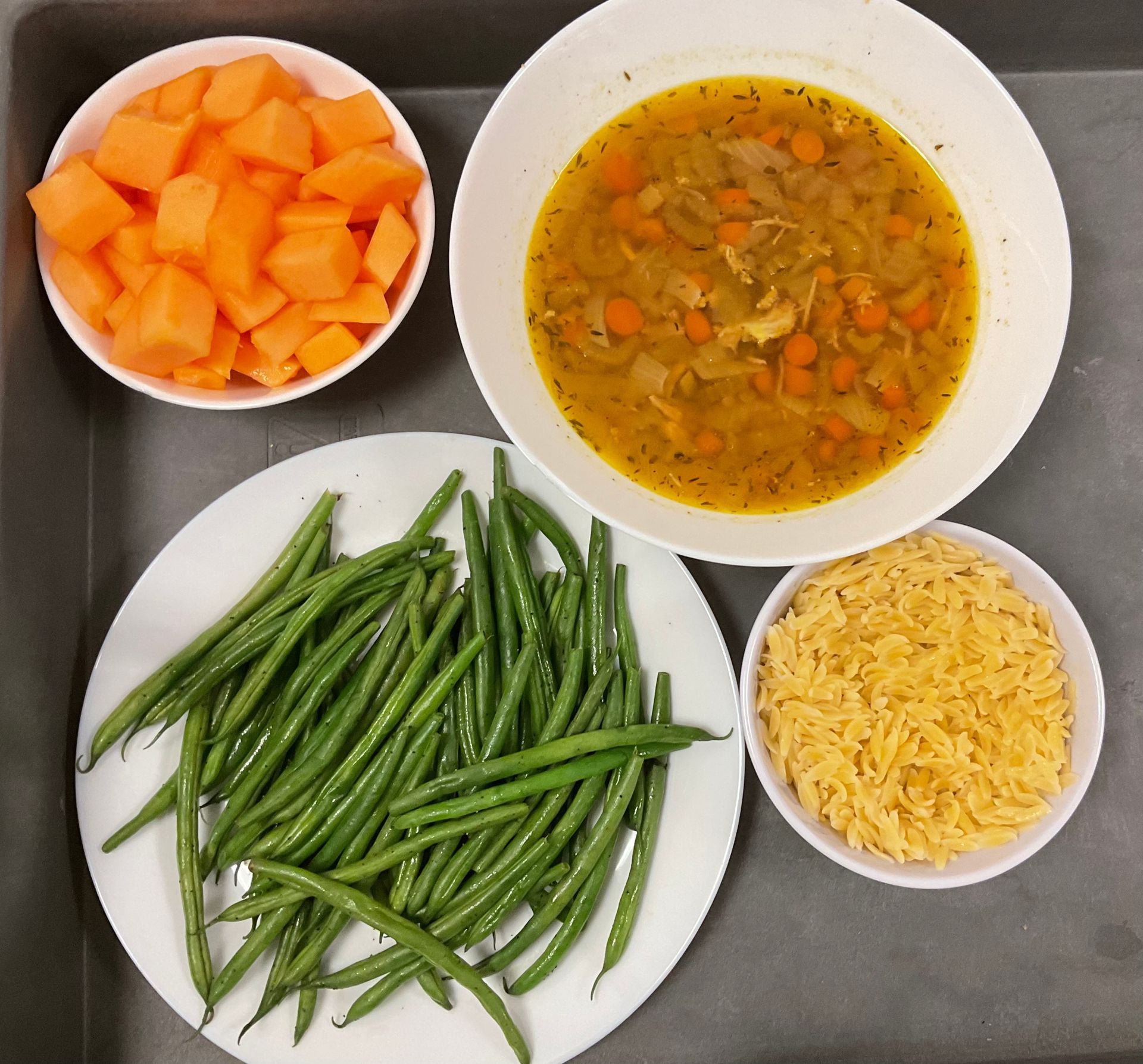 A bowl of soup next to a plate of green beans and a bowl of carrots