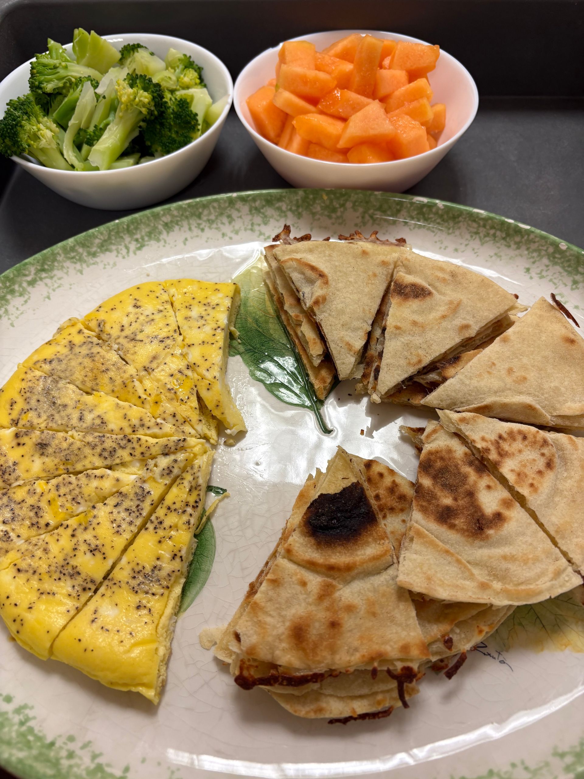 A plate of food with broccoli and cantaloupe on the side