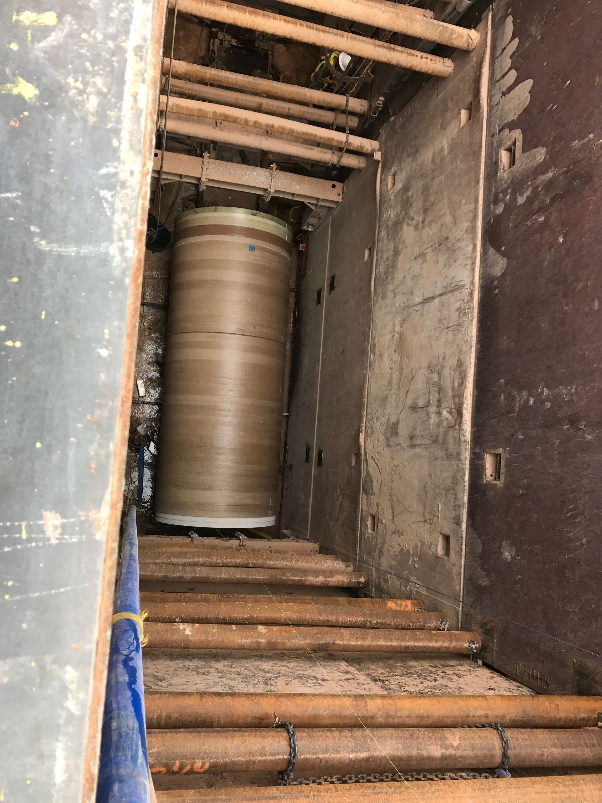 Inside a shaft, a large cylindrical object stands tall. Brown and beige, with metal beams and concrete walls.