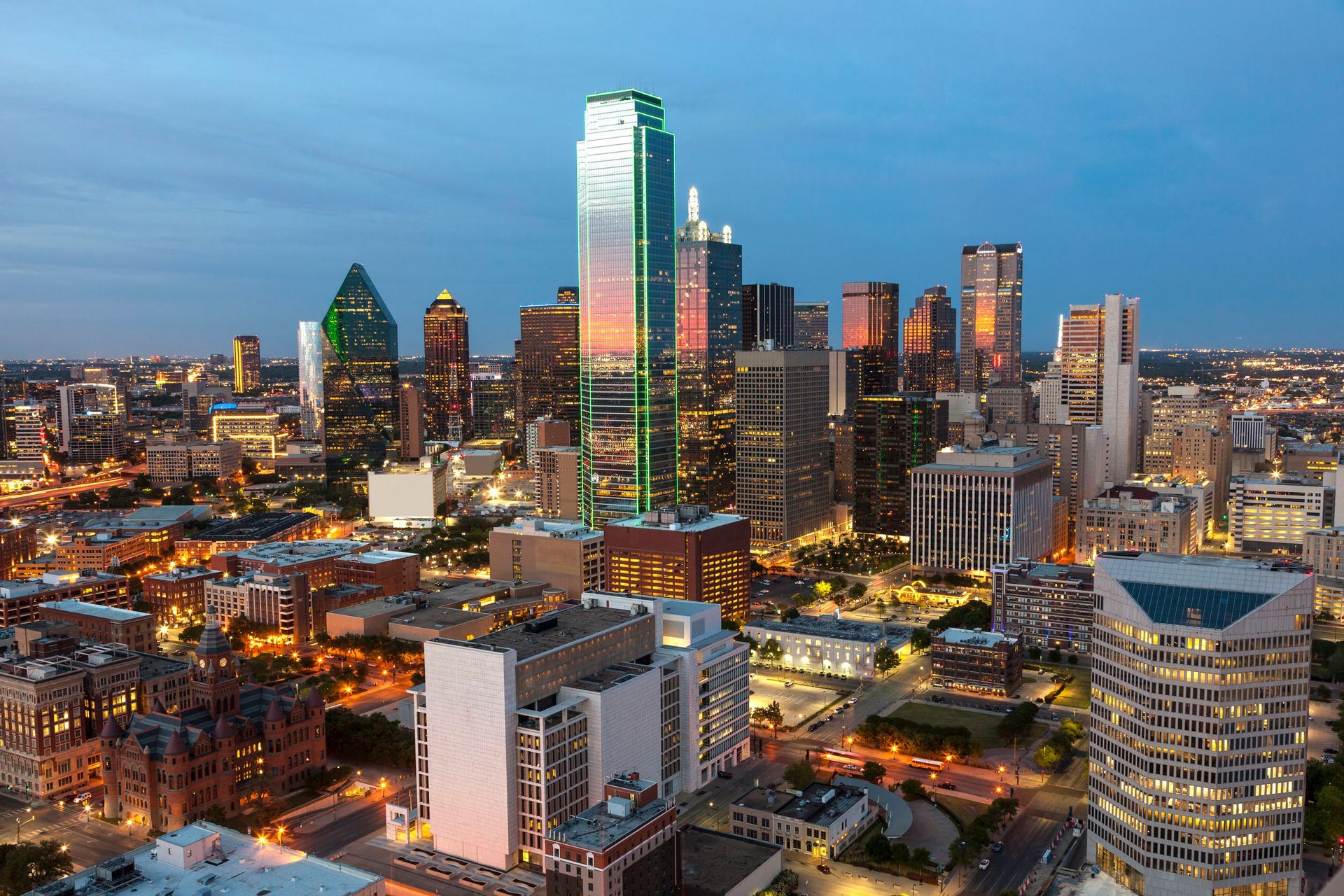 Dallas, Texas skyline at dusk with brightly lit skyscrapers and surrounding city buildings.