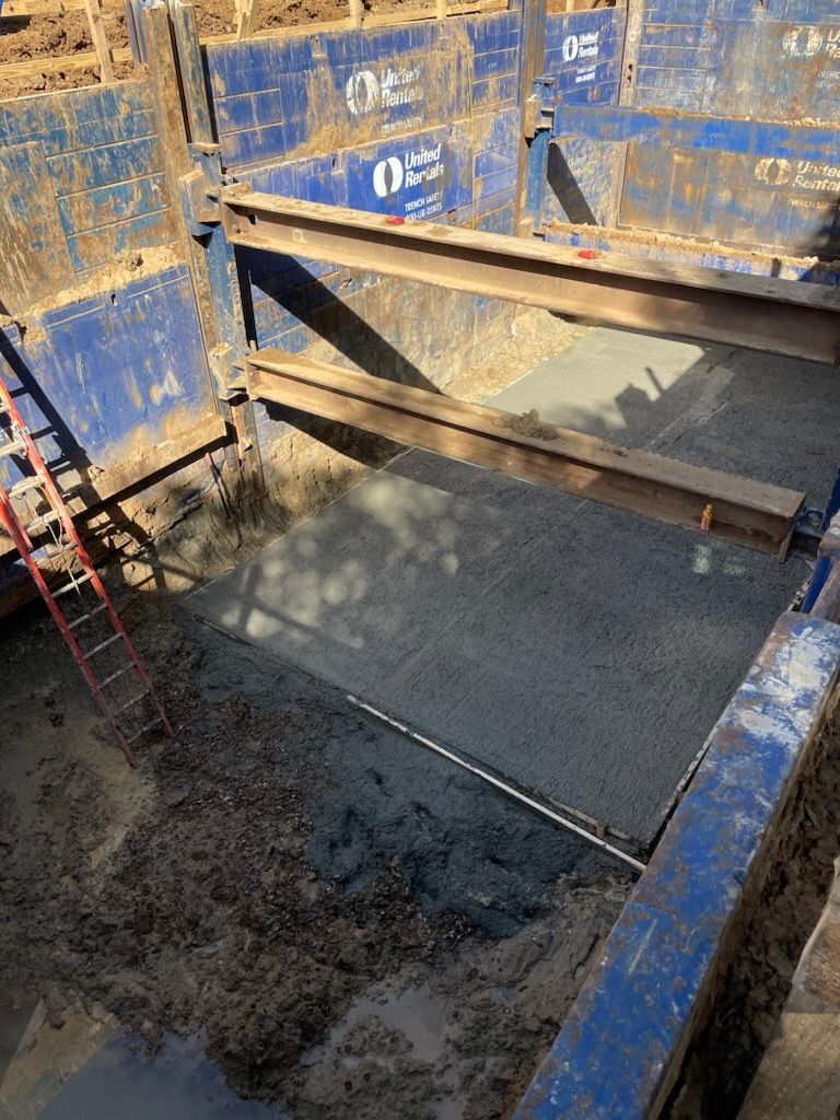Construction site trench with blue supports, ladder, and concrete floor.
