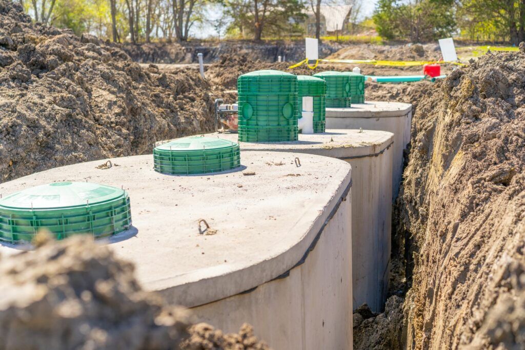 Concrete septic tanks in a trench, with green access lids, surrounded by dirt.