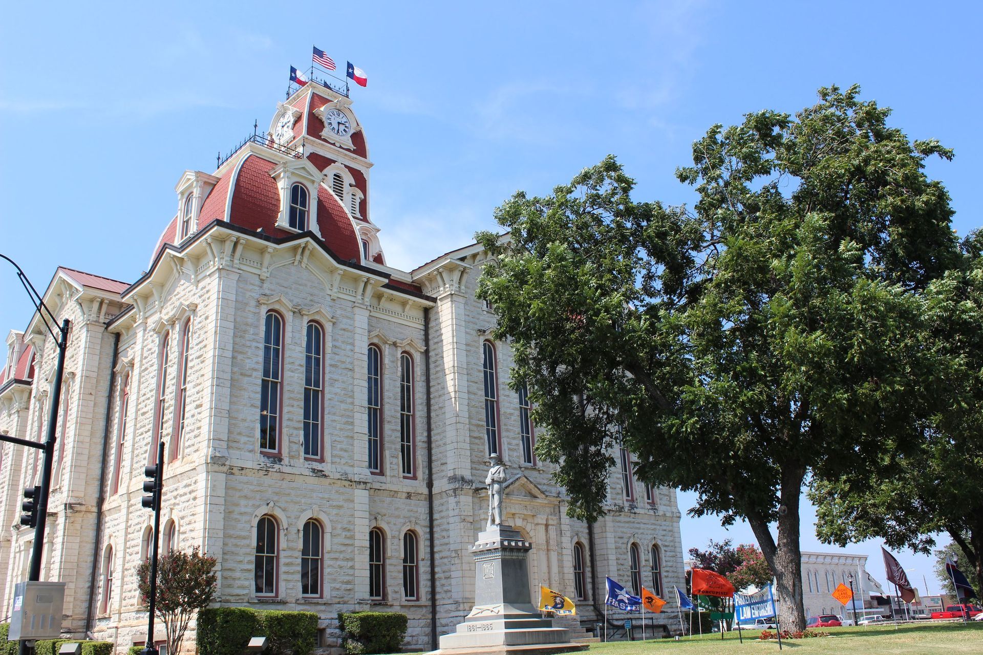 Historic limestone courthouse with a red-roofed clock tower and green trees against a blue sky.