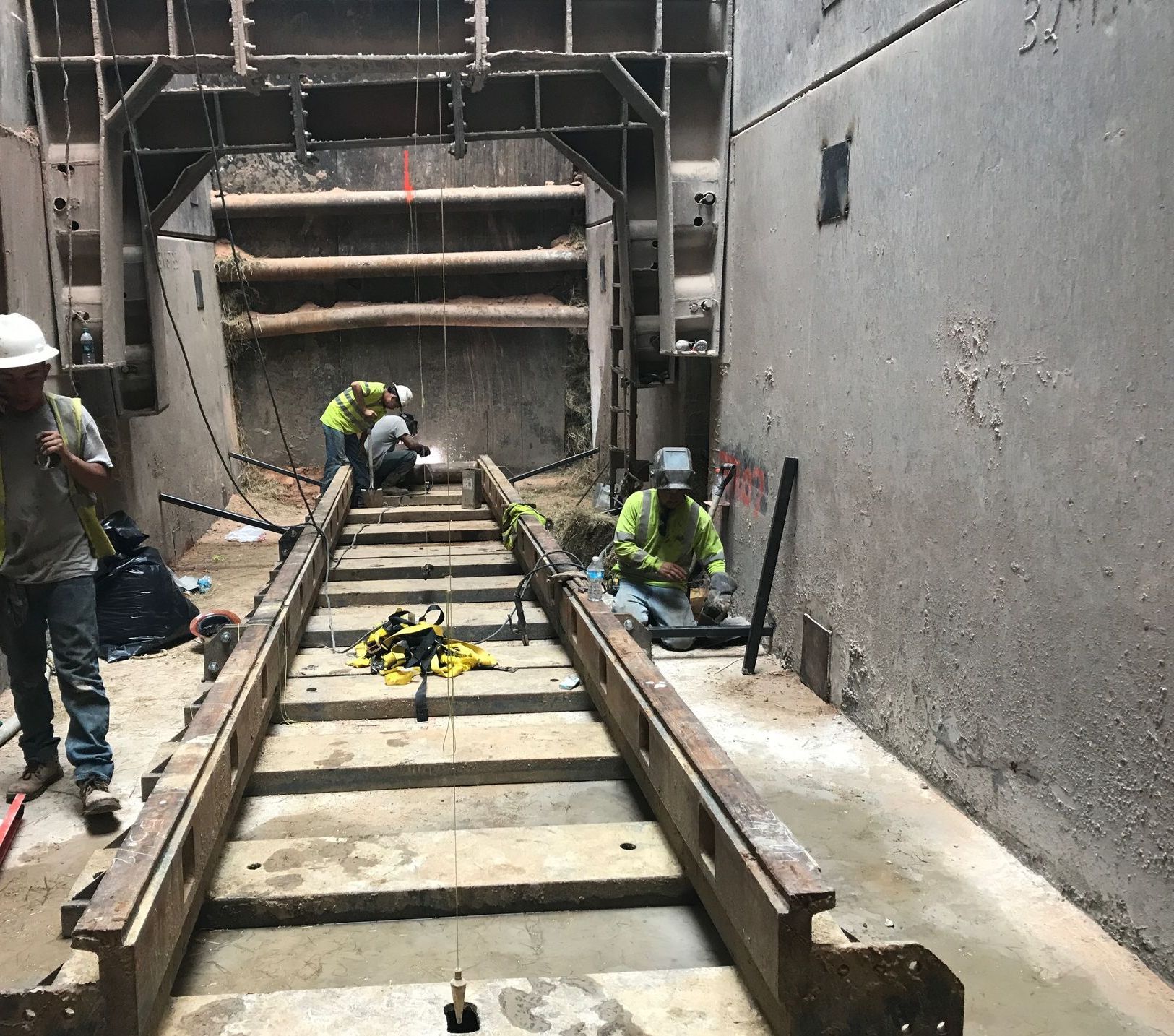 Construction workers inside a concrete tunnel, welding and working on metal tracks.