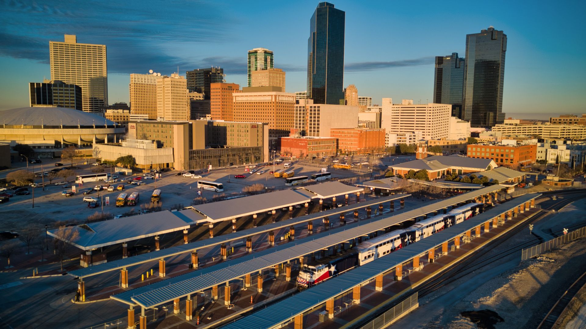 Downtown Fort Worth cityscape with bus station in foreground under blue sky.