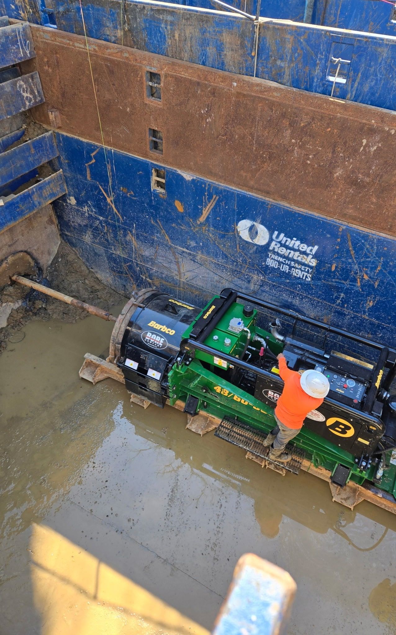 Worker in trench operating a directional boring machine to install utility lines.