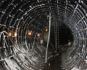 Tunnel interior with black ribbed walls, white substance, and a ladder in the distance.