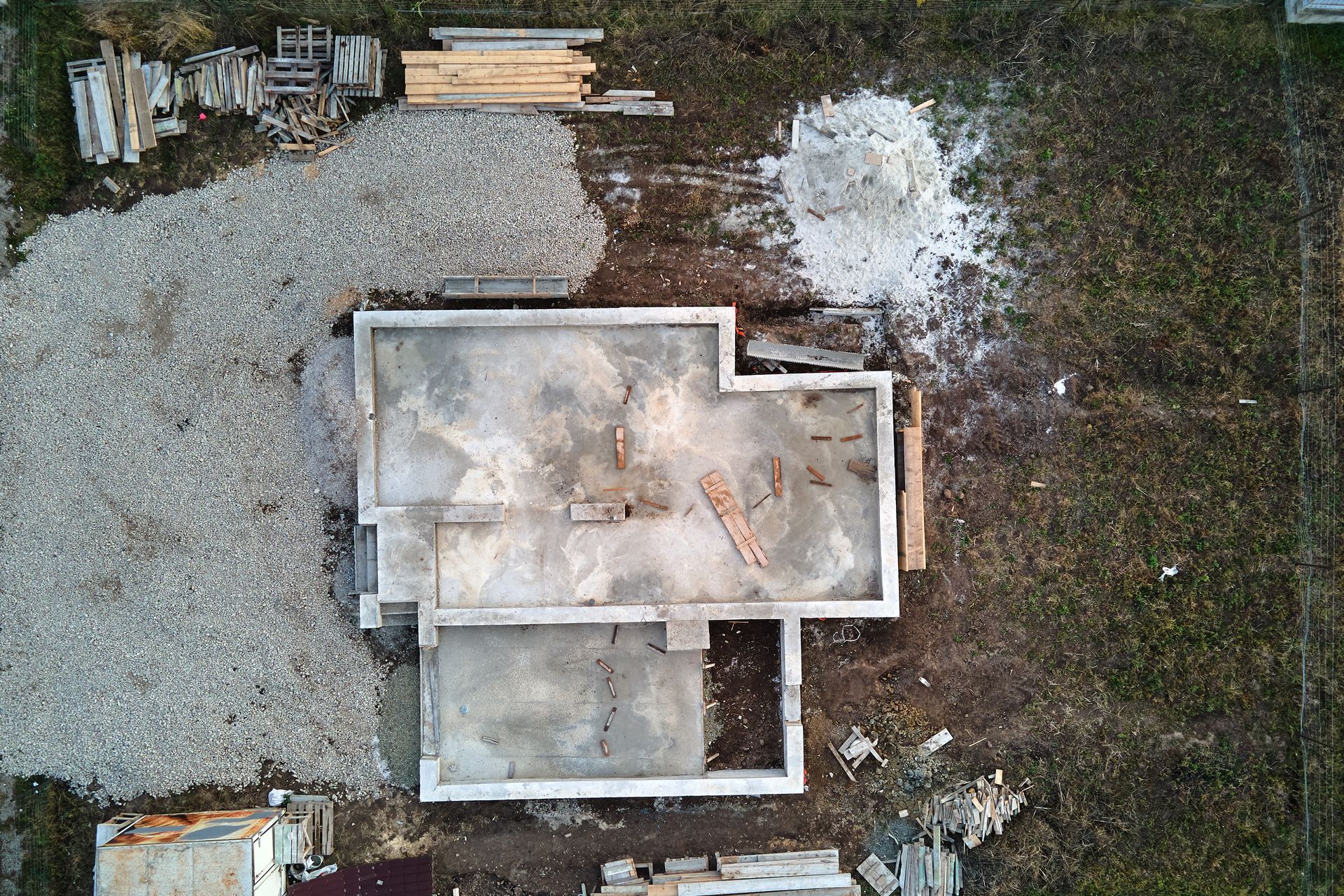 Overhead view of a house foundation under construction with a gravel pile and building materials.