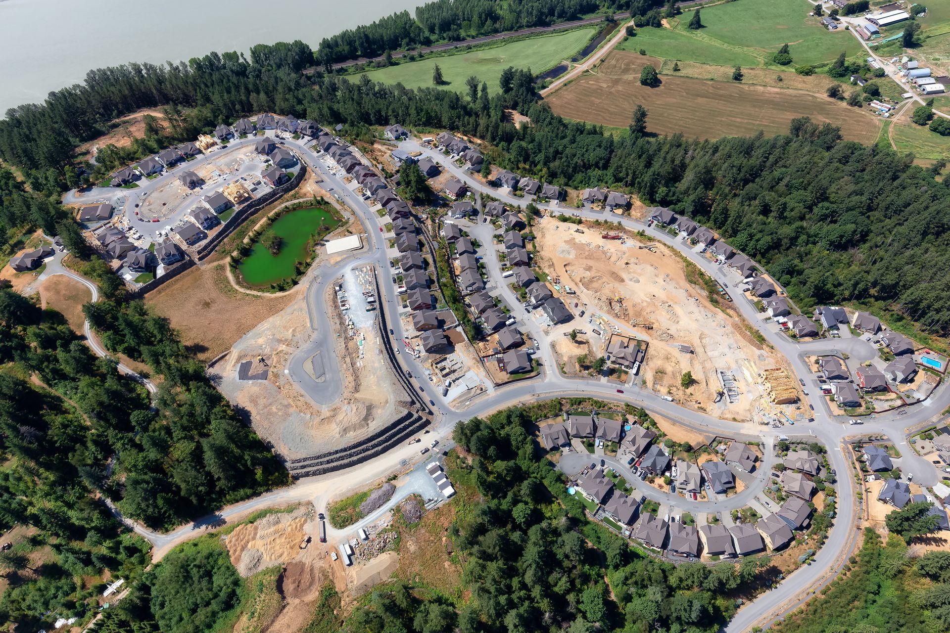 Aerial view of a housing development with various homes, construction, and a small green pond amidst trees.