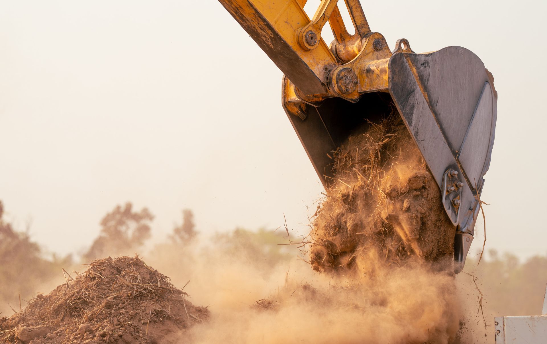 Yellow excavator dumping dirt, creating a dust cloud.