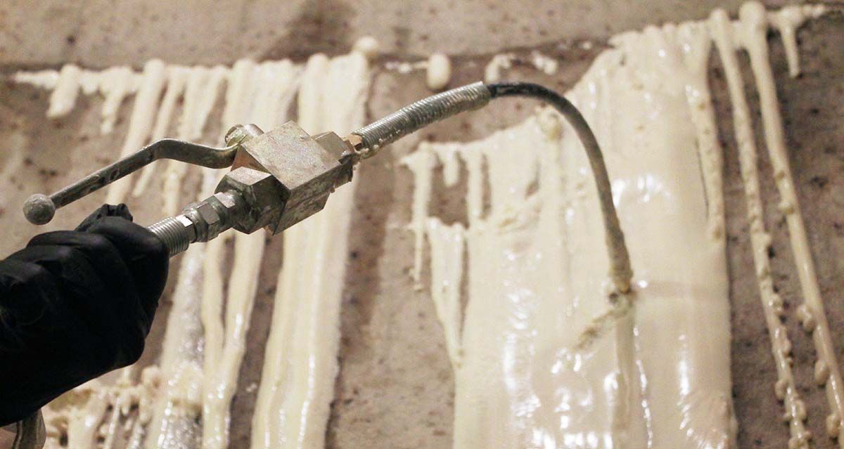 A person sprays a thick, white substance onto a wall with a spray gun, creating dripped patterns.