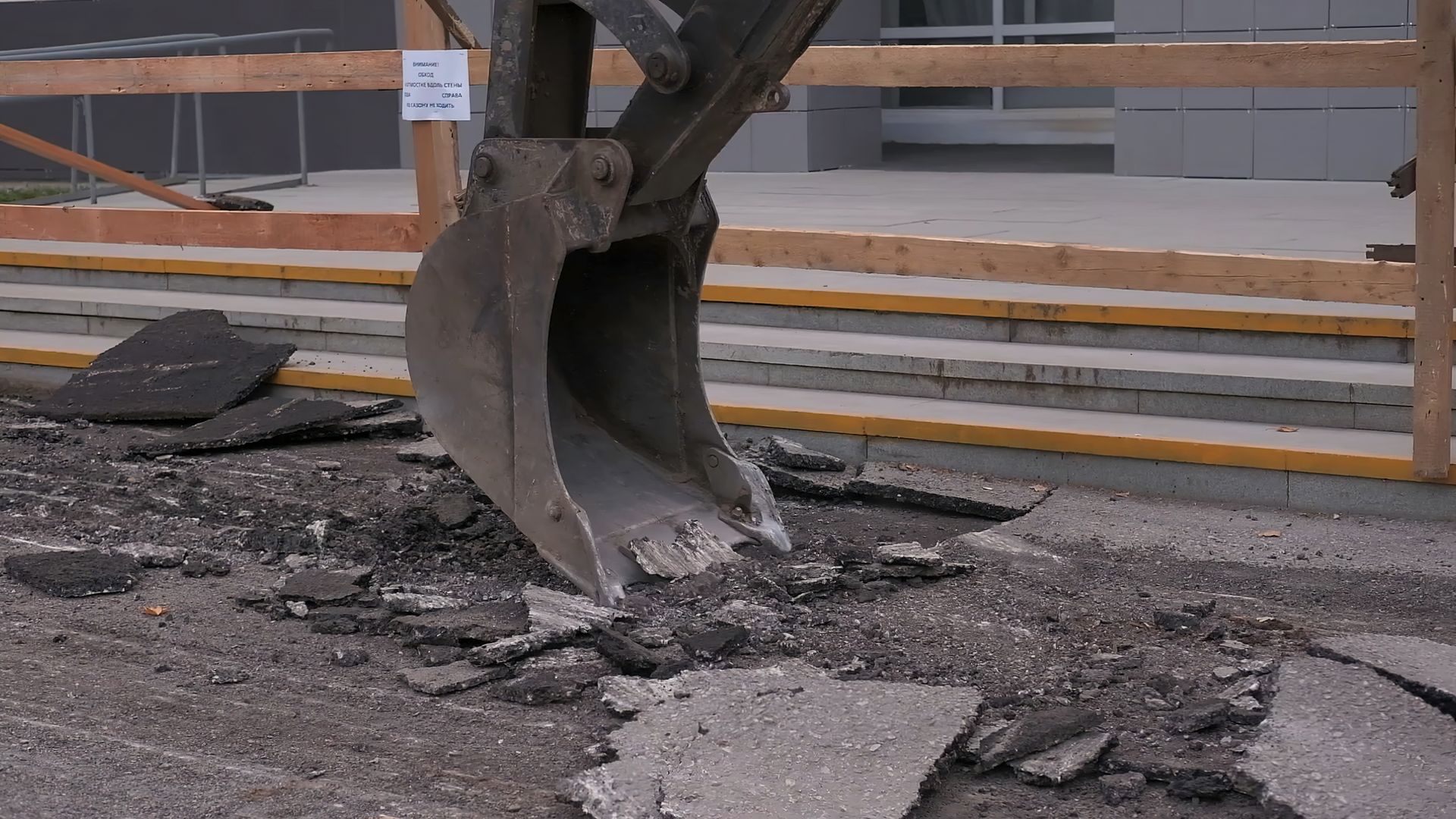 A backhoe bucket tearing up asphalt on a construction site.