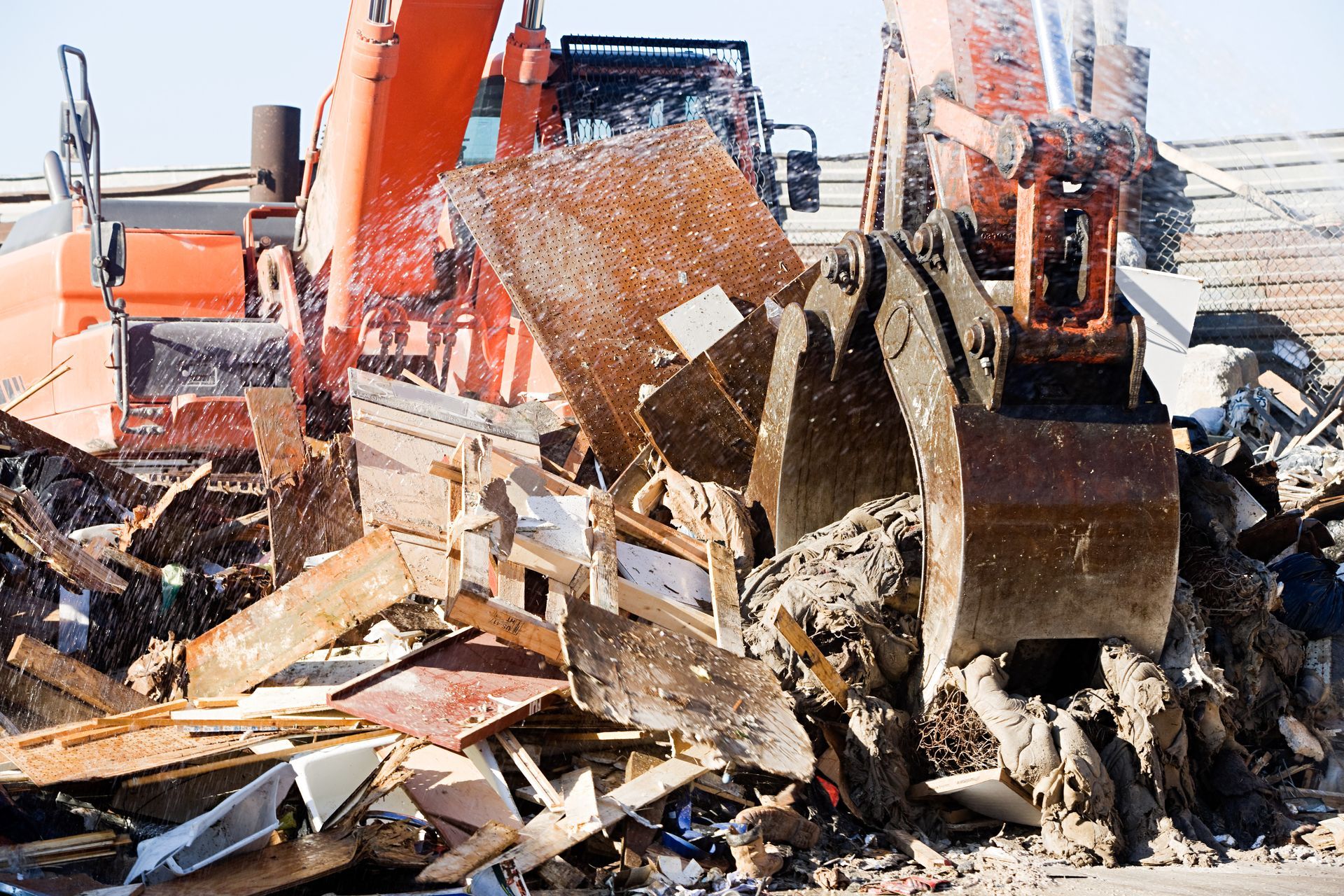Orange excavator demolishing a structure, debris in the foreground.