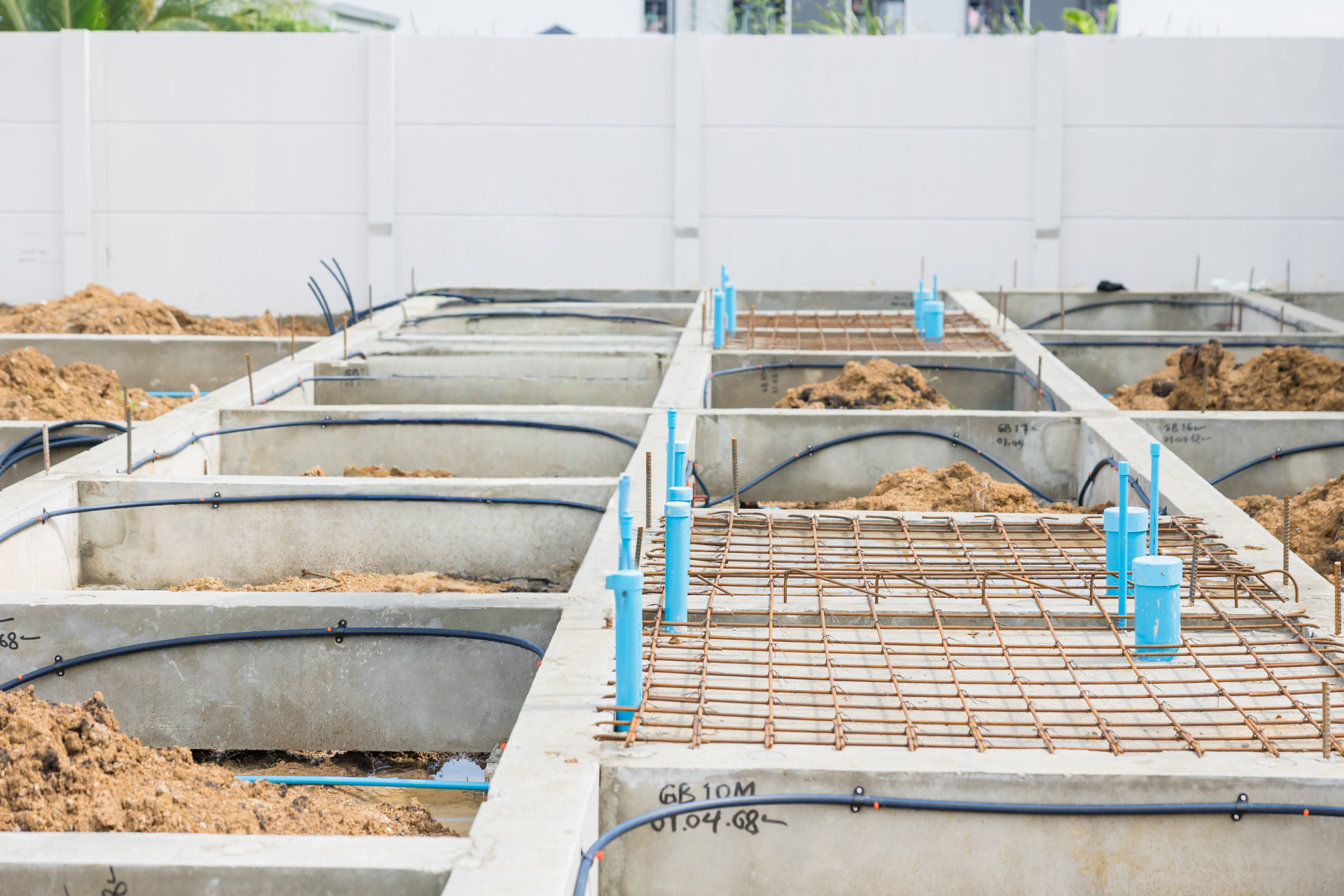 Construction site with concrete forms, rebar, blue pipes, and earth, outdoors.