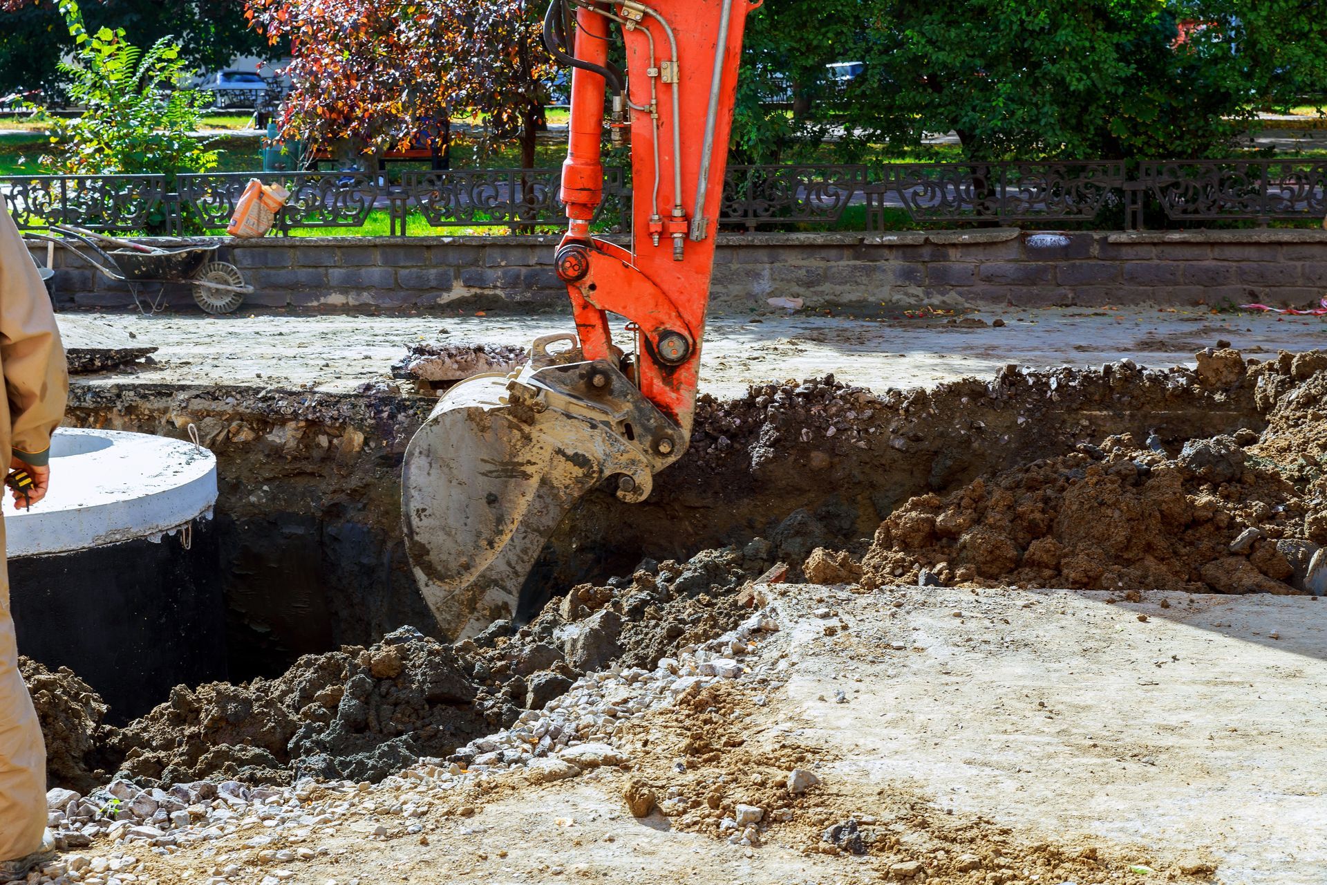 Orange excavator digging near a concrete well in a construction site.