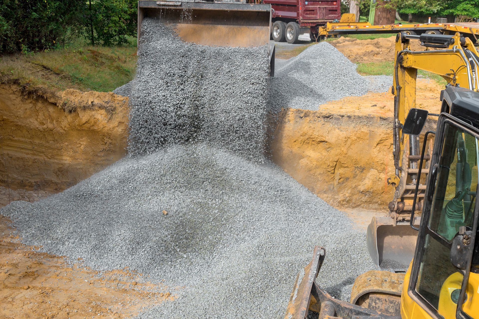 Yellow excavator dumping gravel into a trench, a construction site.