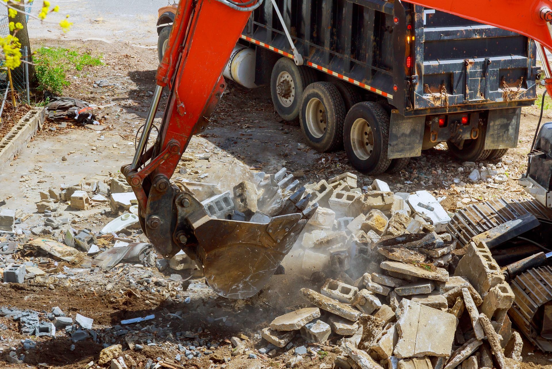 An excavator loads debris into a truck at a construction site; orange, gray, and black.