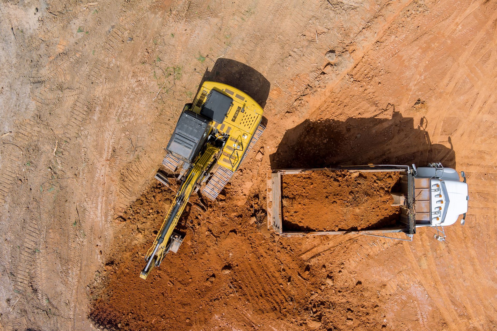 Overhead view of yellow excavator loading dirt into a dump truck at a construction site.