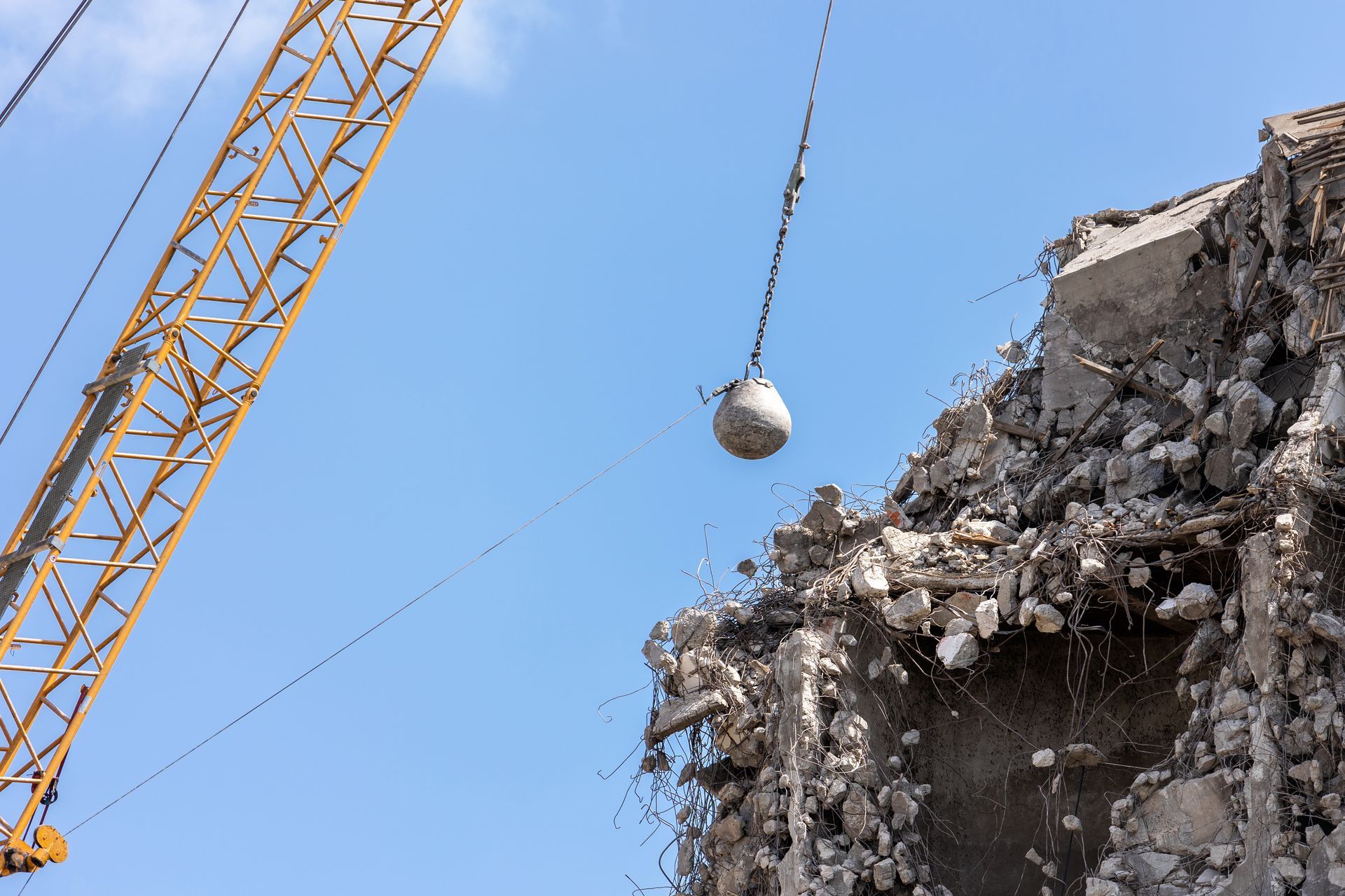 Demolition of a building with a wrecking ball suspended from a crane against a blue sky.