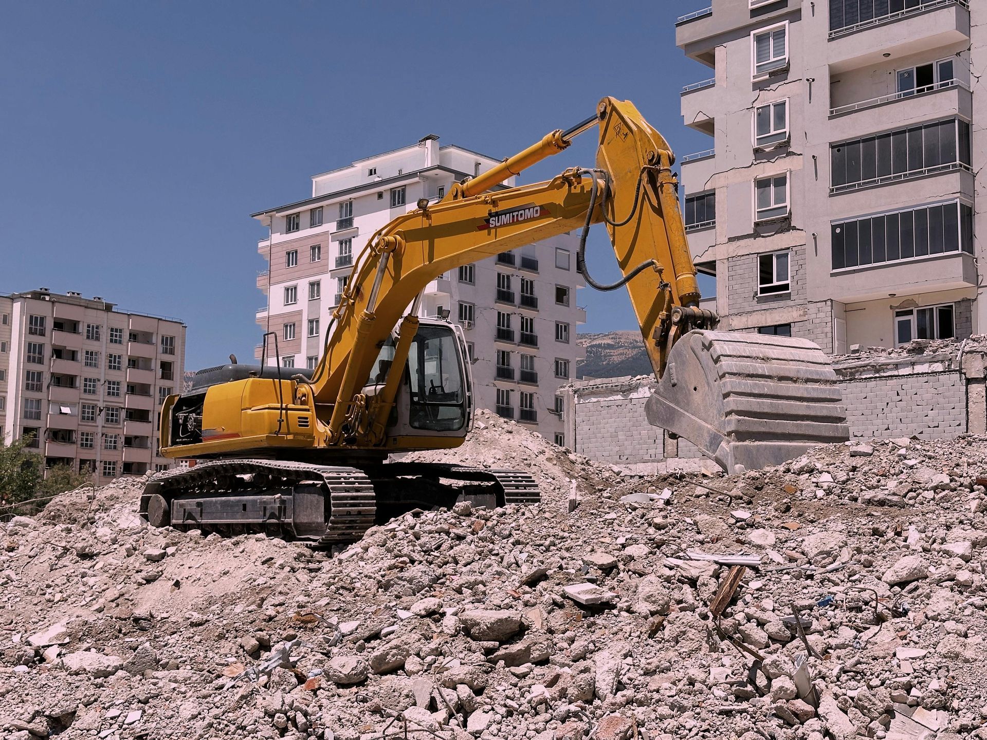 Yellow excavator demolishing a building in a city on a sunny day.