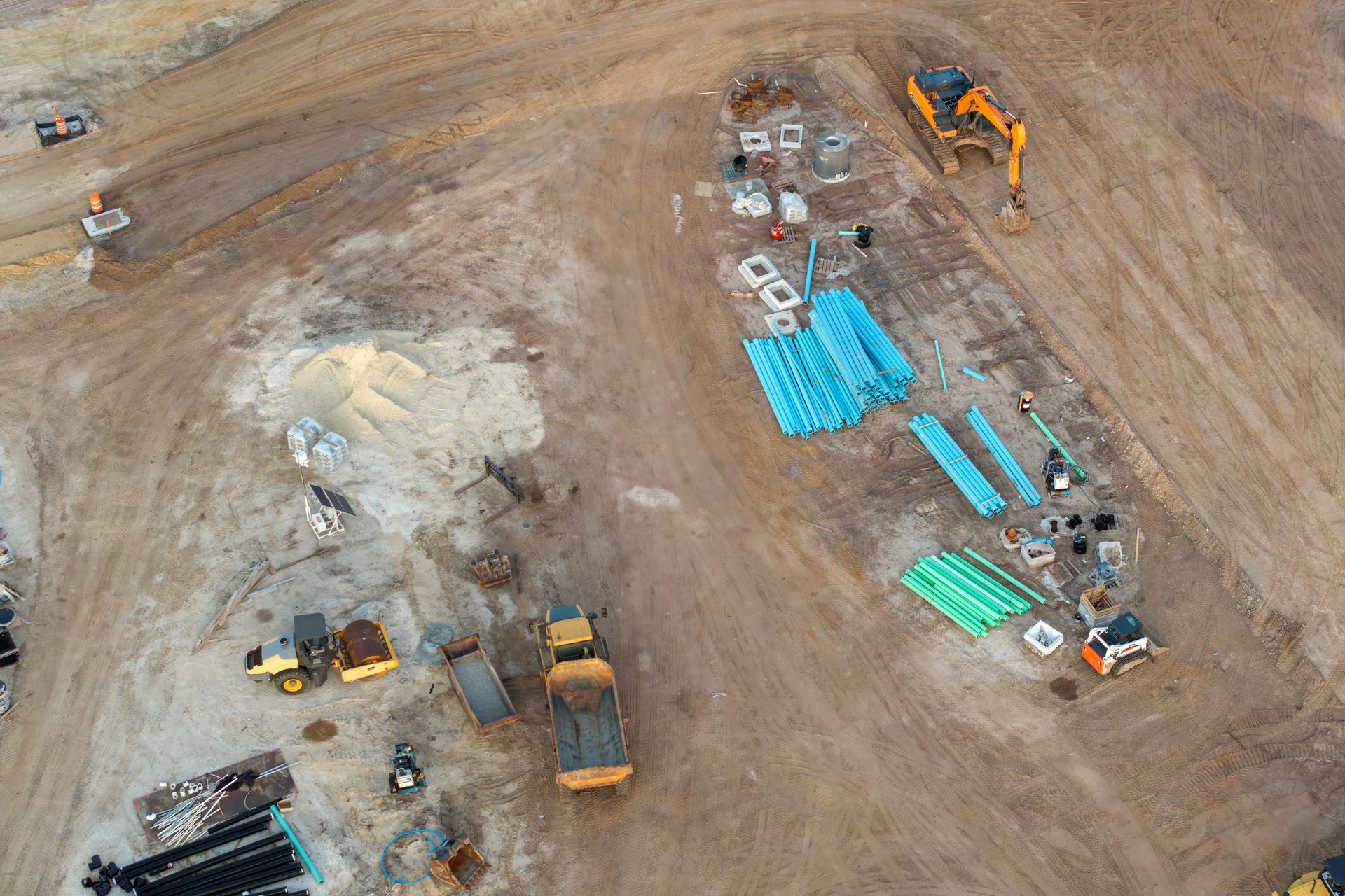 Aerial view of a construction site with heavy machinery, pipes, and materials scattered across the brown earth.