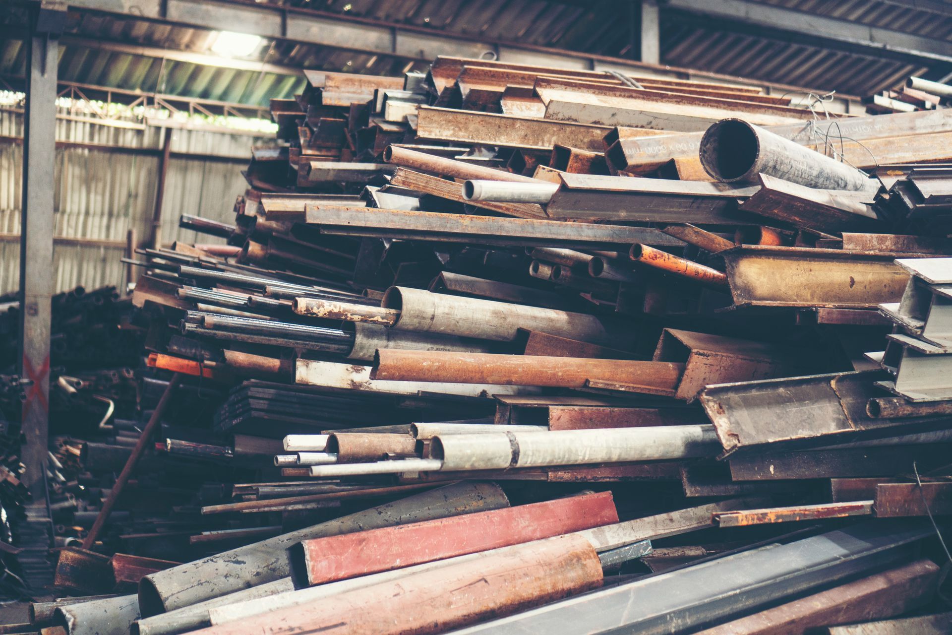 Pile of scrap metal, including pipes and beams, in a warehouse.