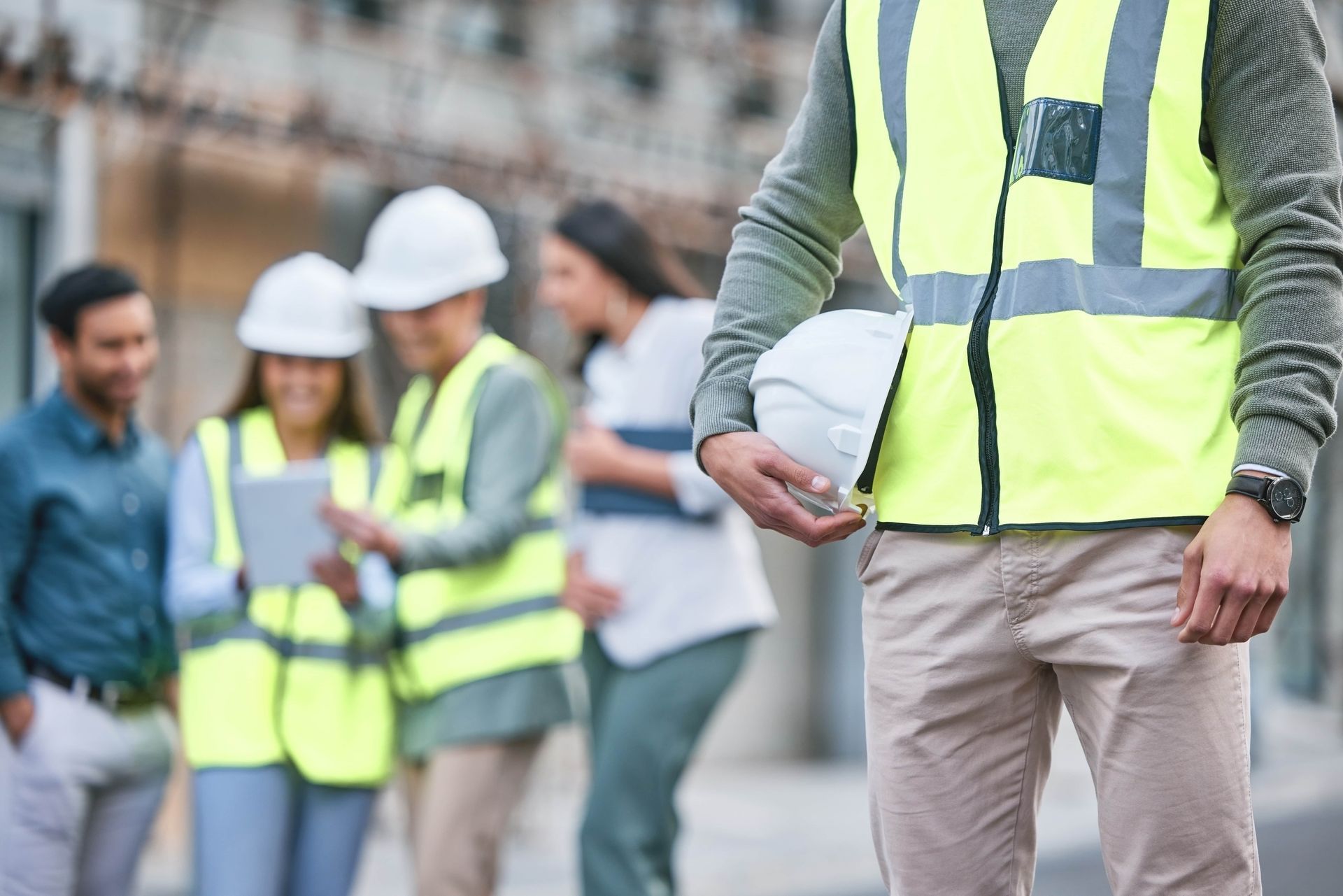Construction workers in yellow vests and hard hats, one holding a helmet, others conversing outdoors.