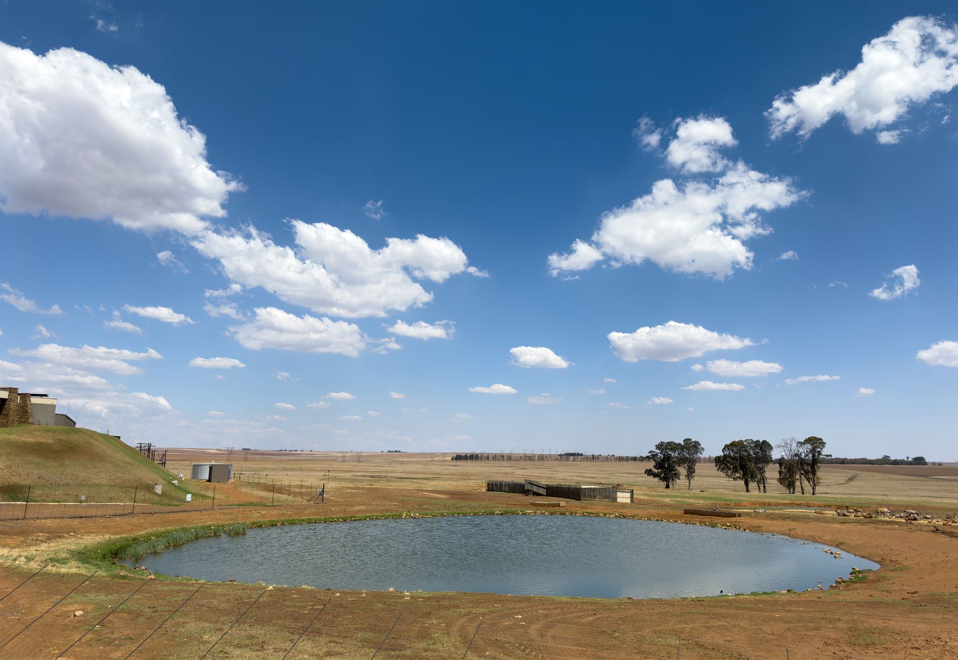 Blue sky with fluffy clouds over a dry, open landscape with a water reservoir.