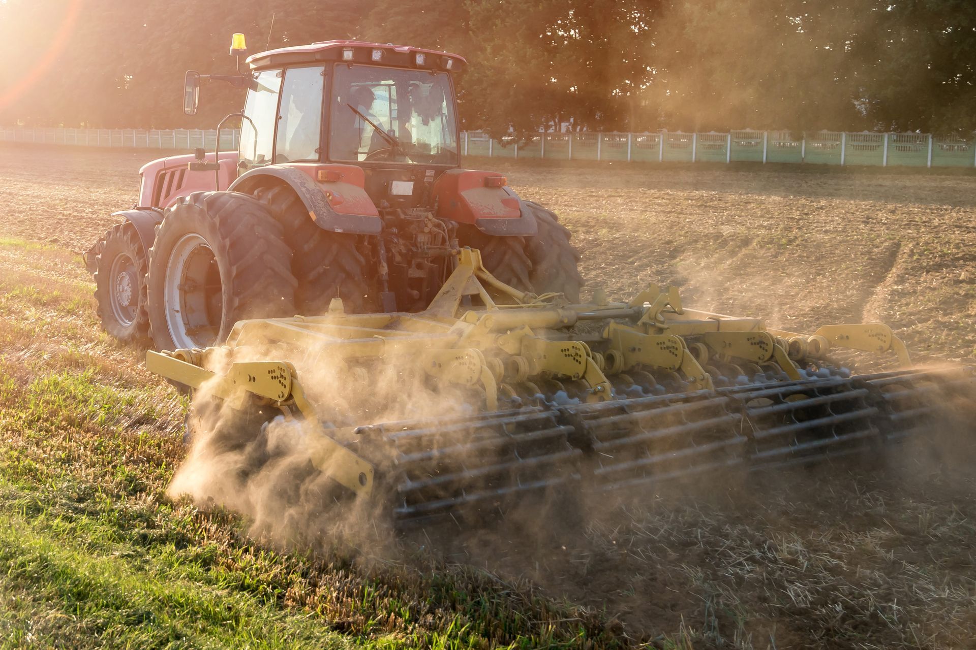 Red tractor plowing a field, kicking up dust in sunlight.