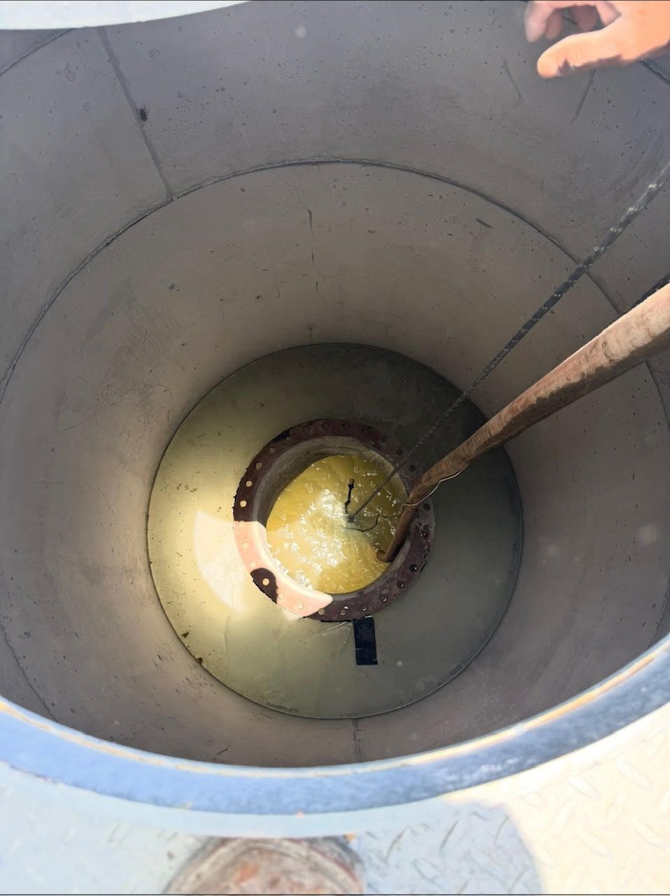 Looking down into a cylindrical tank with liquid inside, a scooping tool is positioned over the liquid.