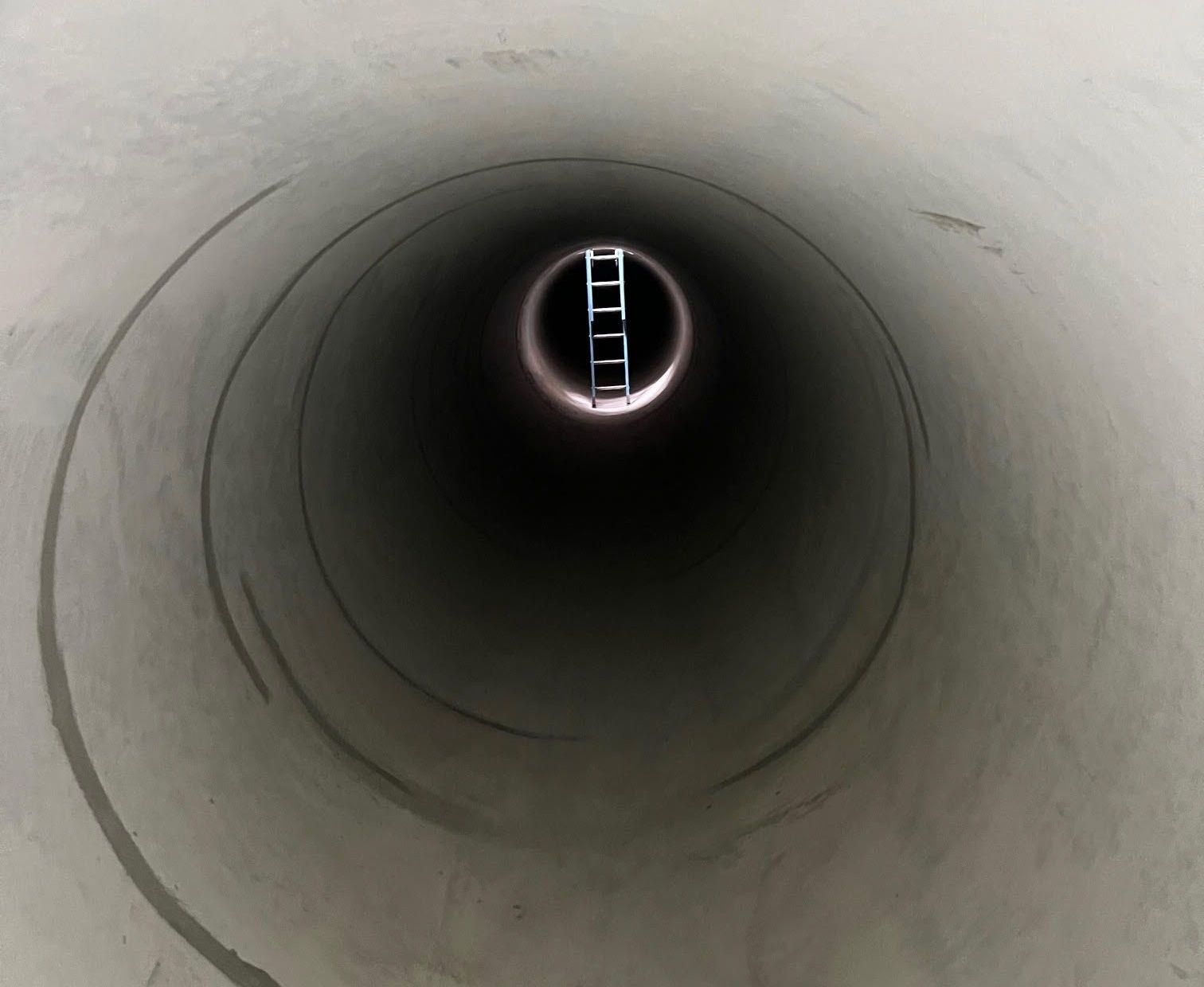 Inside a concrete tunnel, a ladder leads to the distant opening.