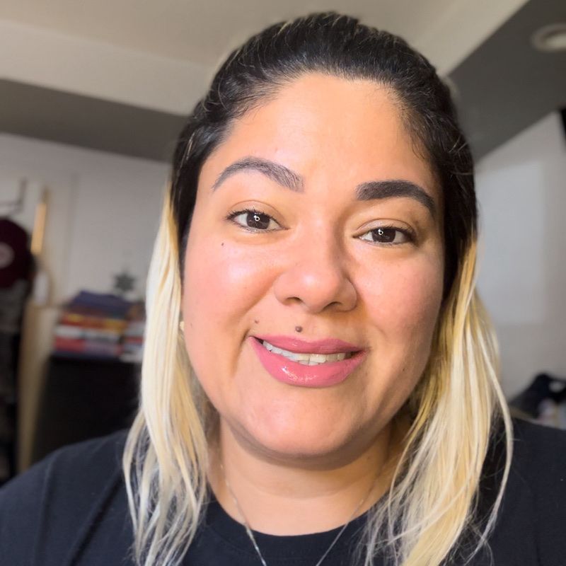 Smiling woman with fair skin, wearing a black shirt. Blonde hair framed her face, with a simple silver necklace.