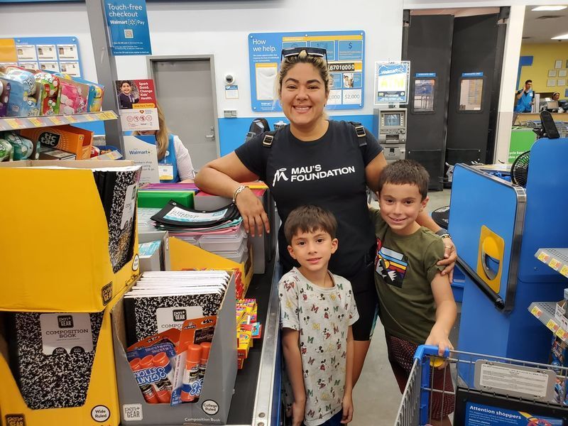 Woman and two young boys smile in a store aisle; they are at a checkout counter, leaning on the conveyor belt.