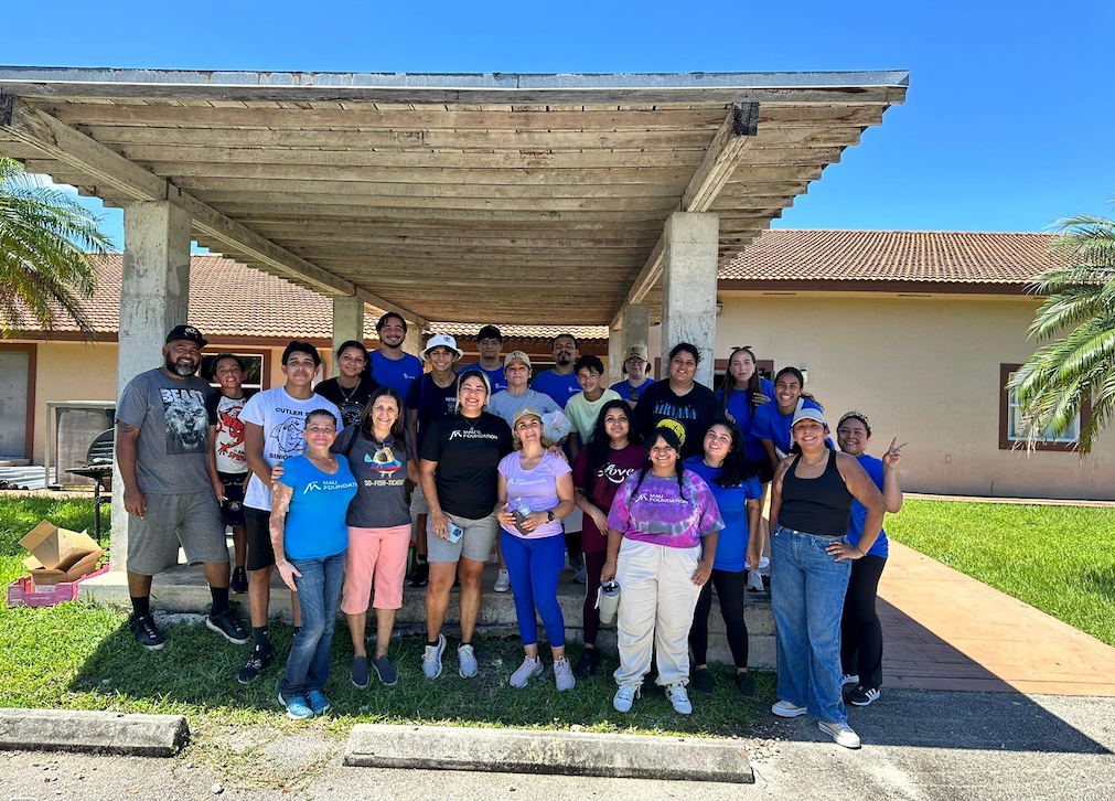 A group of people standing in front of a building with a covered walkway. Many are wearing blue shirts.