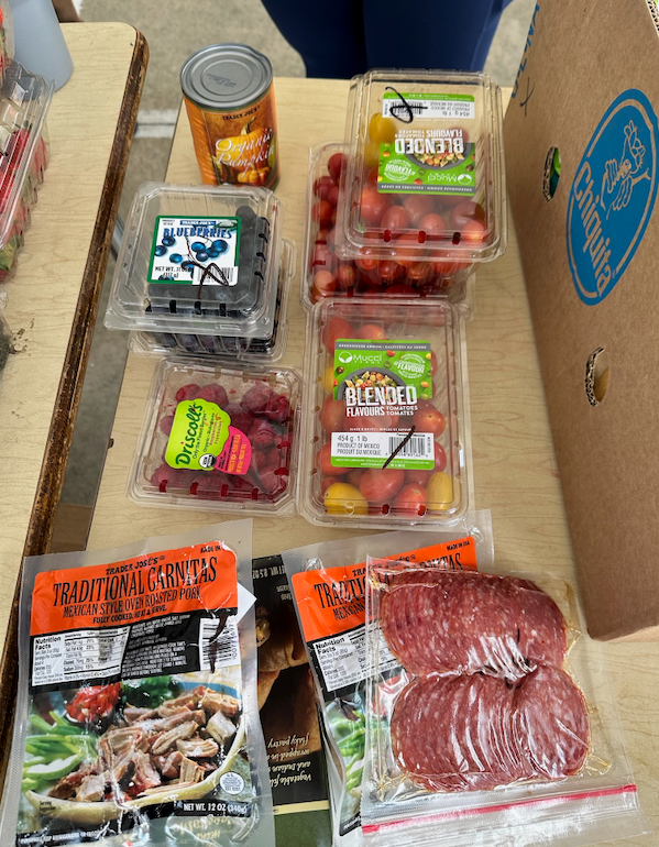 Produce and pre-packaged meats on a table, including berries, tomatoes, and salami. A canned item sits nearby.