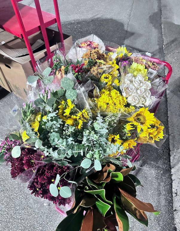 A cart overflowing with a variety of colorful flower bouquets. Sunflowers, yellow, red, and white blossoms are visible.