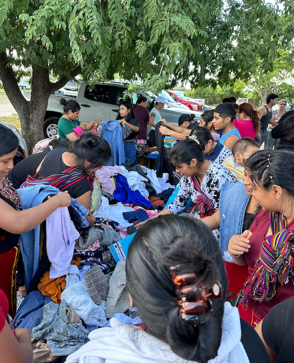 People gathered outdoors, sorting through and selecting clothing from piles on tables, likely a clothing donation event.
