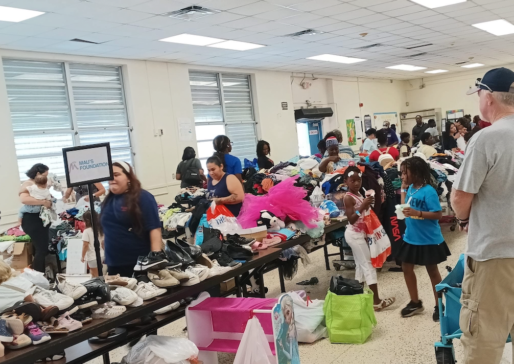 A room filled with people browsing through donated clothes and shoes laid out on tables.